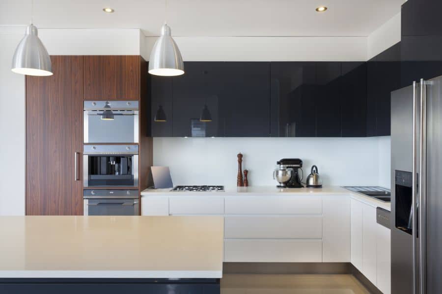 Modern kitchen with black upper cabinets, white lower cabinets, wood paneling, and pendant lights.