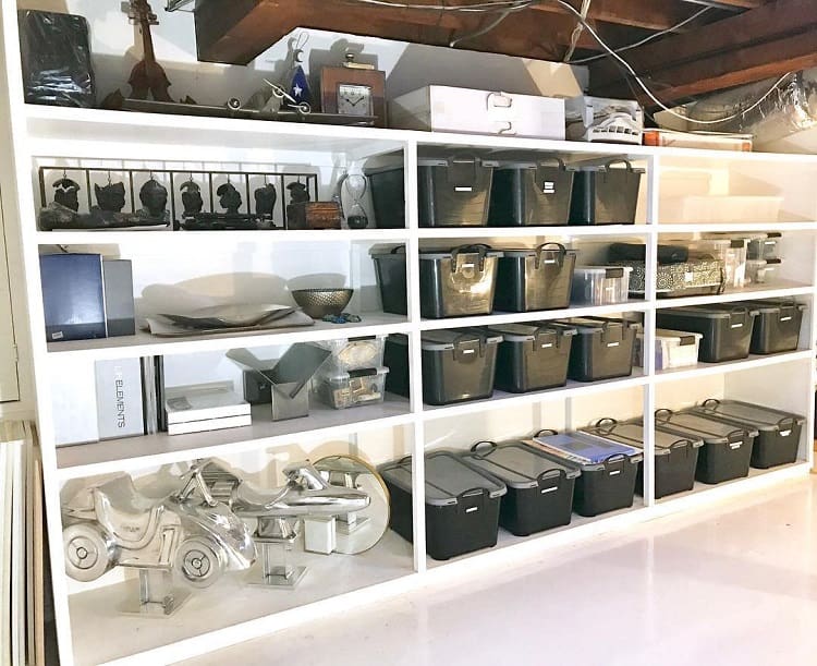White shelves with black storage bins, decorative items, and organized household essentials in a basement.