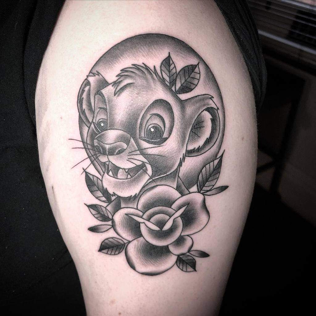 Black and gray tattoo of Simba's face surrounded by leaves and a rose, symbolizing youth and growth