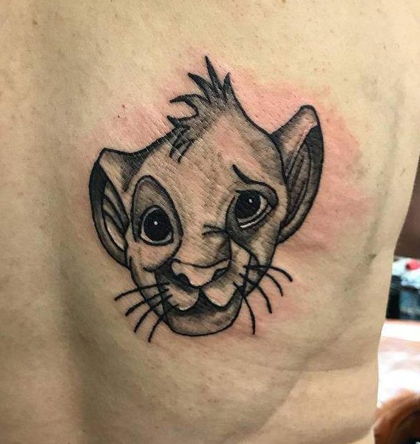 Black and gray tattoo of Simba's face with a playful expression, highlighting his innocence and charm