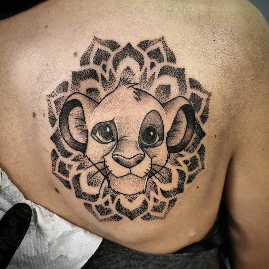 Black and gray tattoo of Simba's face surrounded by intricate mandala patterns, symbolizing strength and harmony