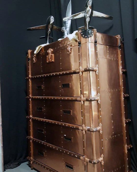 Large copper storage trunk with rivet details and airplane decor on top in a modern setting.