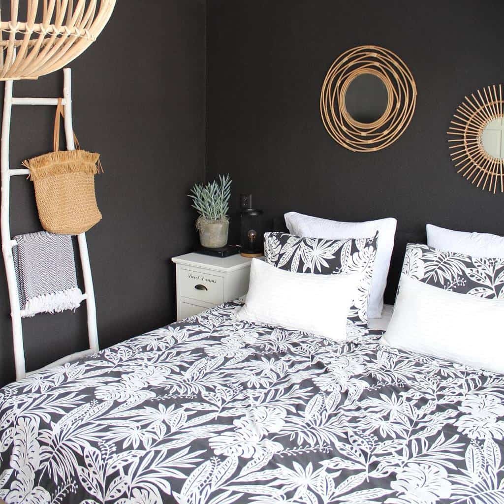 Black accent wall bedroom with tropical-patterned bedding, wicker mirrors, and ladder decor.