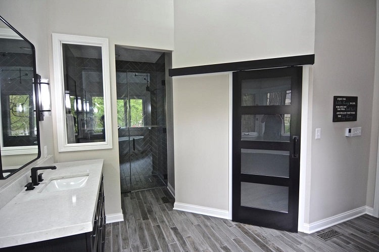Black sliding barn door with frosted glass panels in a modern bathroom with grey tile flooring.