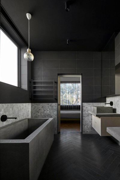 Minimalist black bathroom with concrete bathtub, herringbone flooring, and modern fixtures.