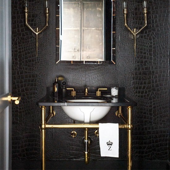 Bathroom with black textured walls, gold accents, and a vintage-style mirror.