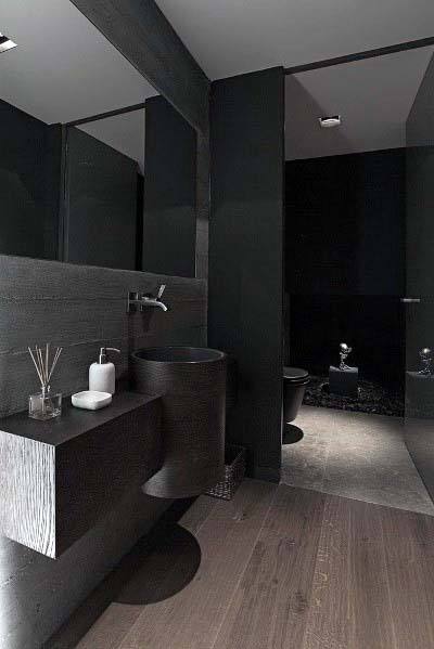 Minimalist black bathroom with wood accents, cylindrical sink, and soft ambient lighting.