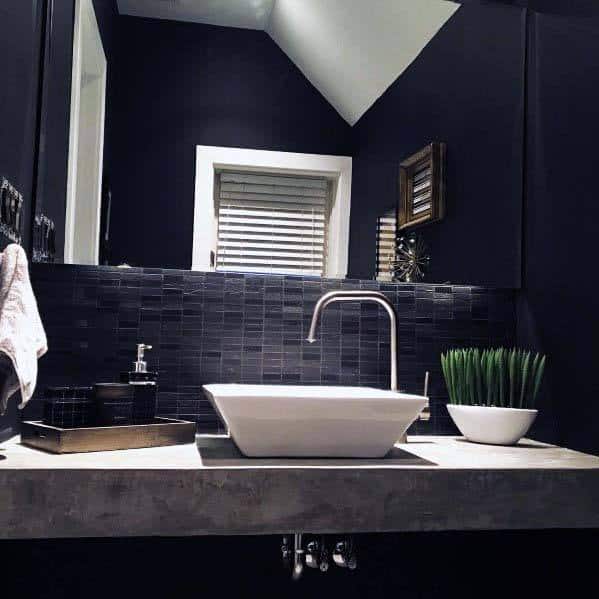 Modern black bathroom with vessel sink, concrete countertop, and decorative greenery.