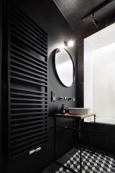 Contemporary black bathroom with geometric floor tiles, round mirror, and sleek radiator.