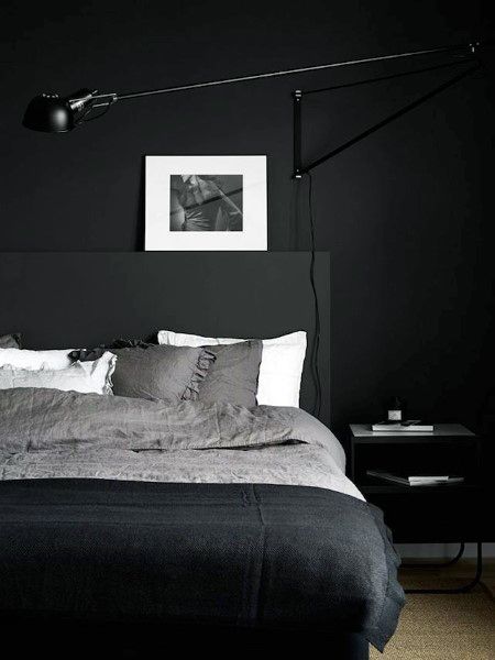 Minimalist black bedroom with textured bedding, wall-mounted lamp, and monochrome artwork.