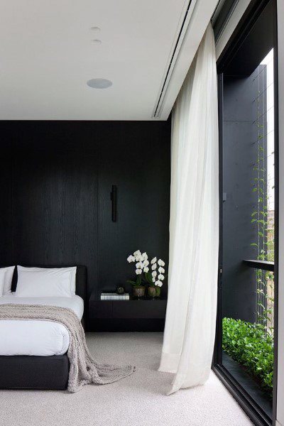Modern black bedroom with floor-to-ceiling windows, sheer curtains, and elegant orchid decor.