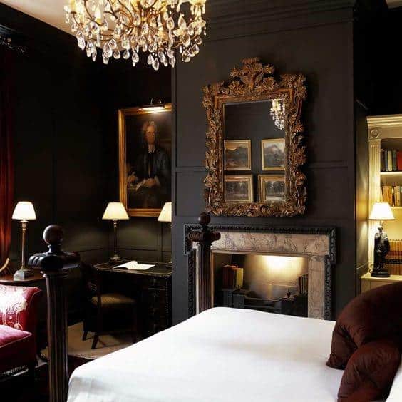 Luxurious black bedroom with ornate gold mirror, crystal chandelier, and vintage fireplace.