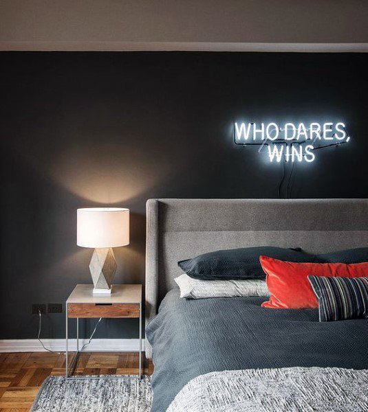 Modern black bedroom with neon wall sign, gray upholstered bed, and stylish bedside lamp.