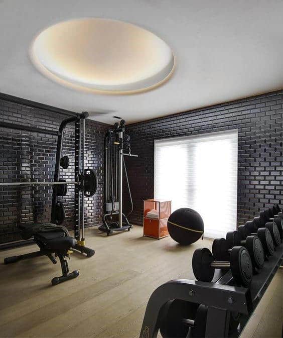 Home gym with black brick walls, dumbbells, yoga ball, exercise machine, and a round skylight in your cozy home