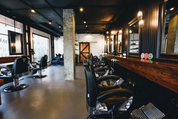 Barbershop with industrial design, featuring black ceilings, a polished concrete floor, and a rustic wooden counter.