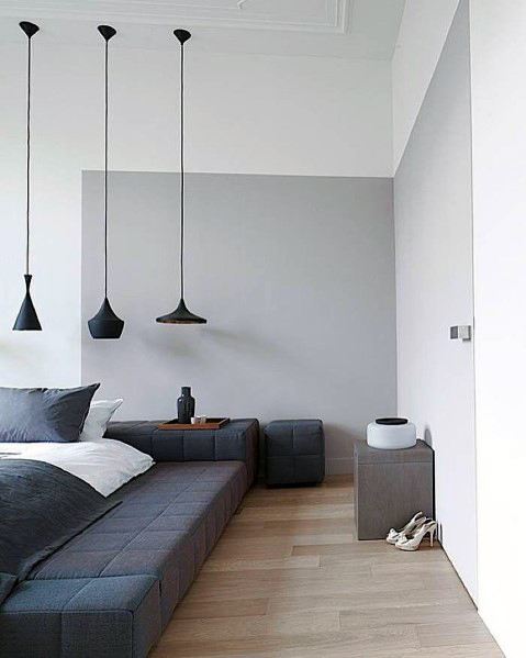 Minimalist bedroom with low platform bed black pendant lights and gray accent wall.