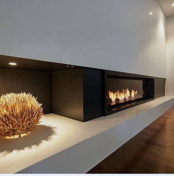 Modern black fireplace with decorative lighting and wooden accent piece on a white shelf.