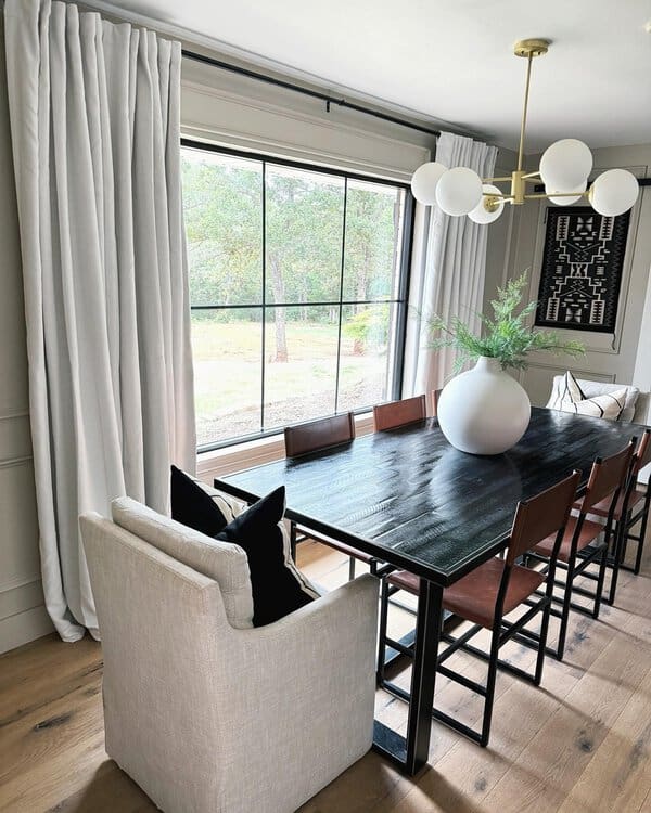 Modern dining room with white blackout curtains, a black table, leather chairs, and a gold chandelier.
