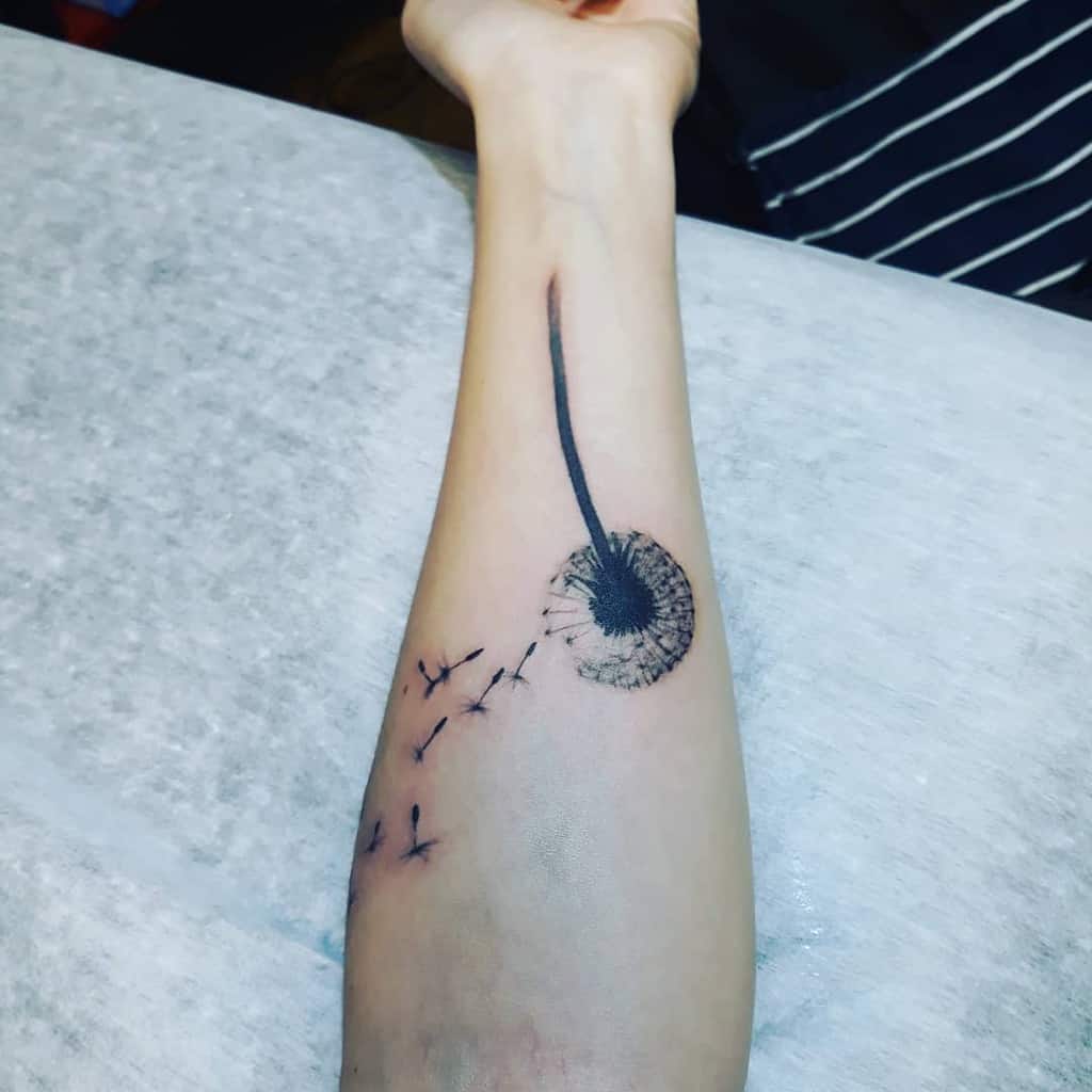 A simple dandelion tattoo on the forearm, with delicate seeds drifting away, symbolizing freedom and letting go.