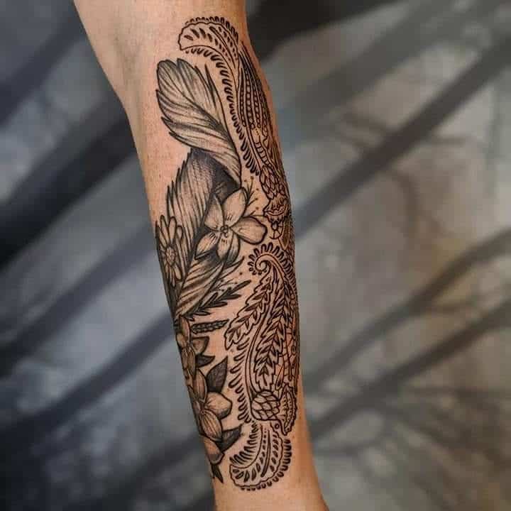 Elegant forearm tattoo featuring intricate lace-inspired paisley patterns, delicate flowers, and fine shading for a soft yet bold look.