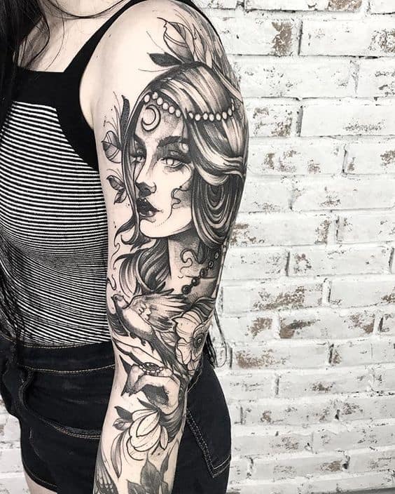 Black and grey full-sleeve tattoo of a mystical gypsy woman with flowing hair, floral details, and intricate shading.
