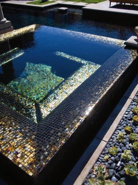 Luxurious pool with black and gold iridescent mosaic tiles, surrounded by succulents and pebbles.