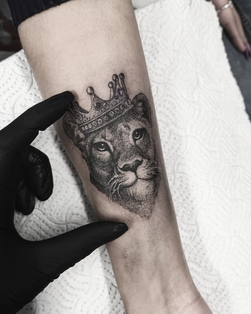 Small black and grey lioness tattoo on the forearm, featuring a detailed crown and fine shading for a regal and elegant design.