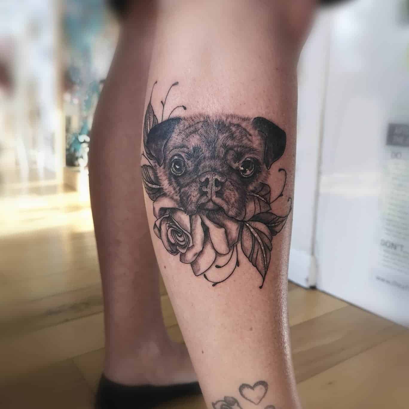 Black and grey tattoo of a realistic pug's face with roses and leaves 