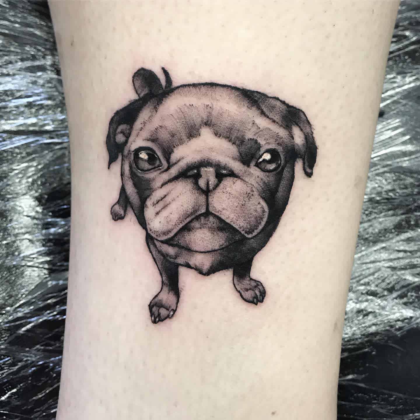 Black and gray tattoo of a small pug with a large head, featuring detailed shading