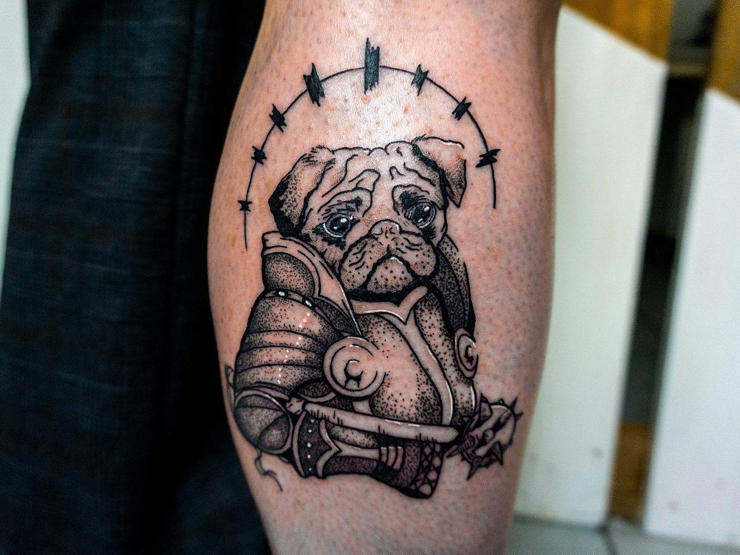 Tattoo of a pug wearing medieval knight armor holding a morning star, with a circular halo design above its head