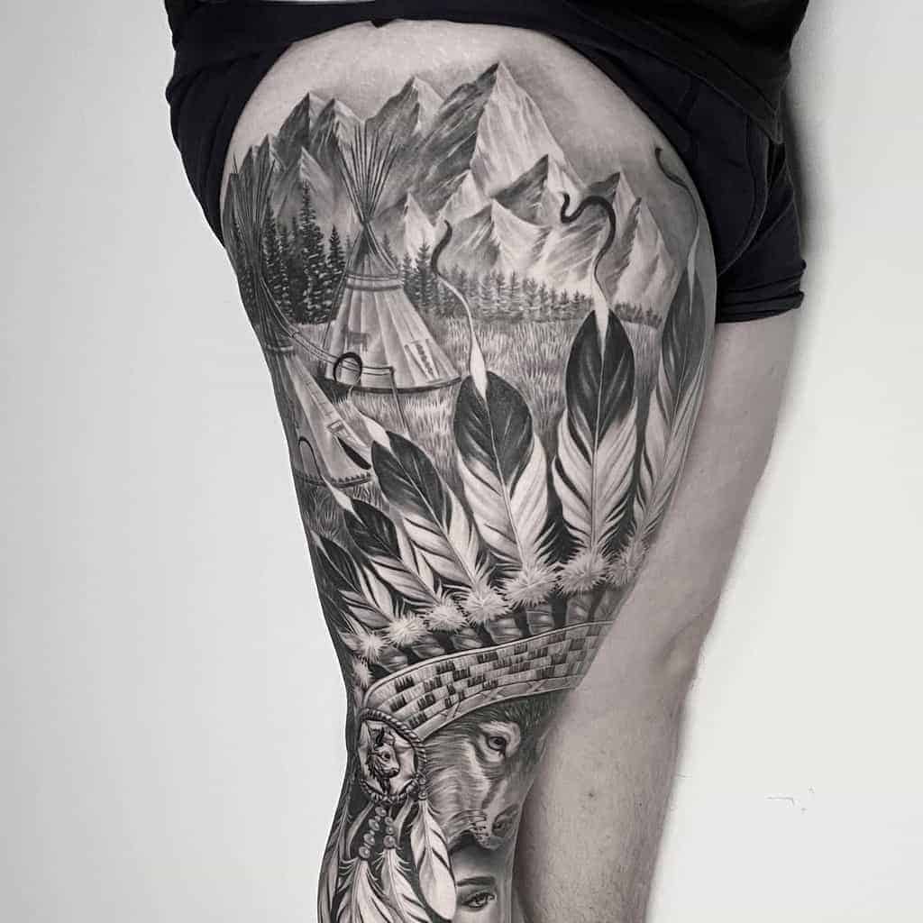 Indian tattoo of mountains, wildlife, feathers, and a tipi covering a person's thigh