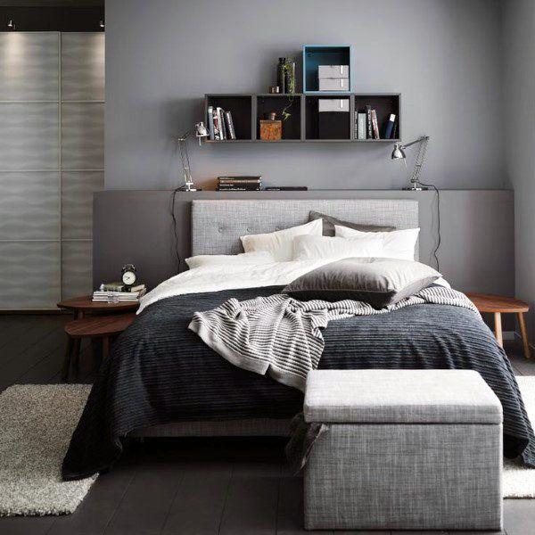 Modern bedroom with a chic grey bed, layered bedding, wall-mounted shelves, and sleek lamps on side tables
