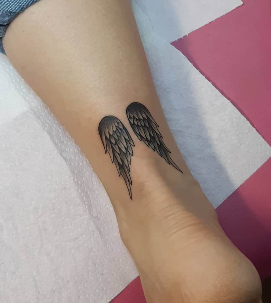 Tattoo of two small black angel wings, with feathered details
