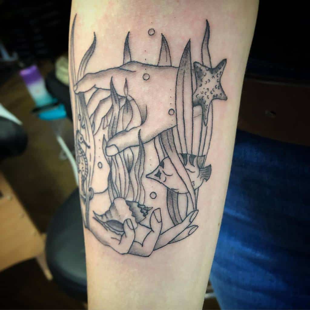 Detailed ocean-themed tattoo featuring hands, seaweed, fish, a starfish, sea horse and seashells in a surreal composition