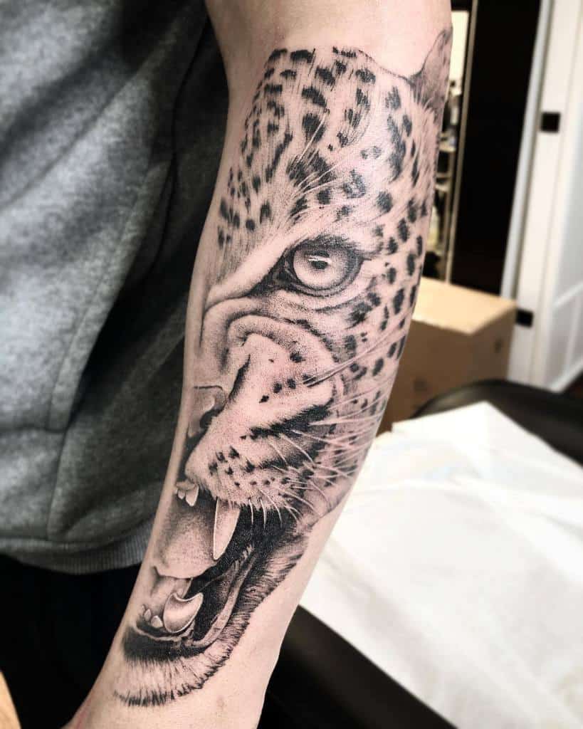 A detailed black and grey tattoo of a jaguar’s roaring face, wrapping around the forearm with intense shading and lifelike features.