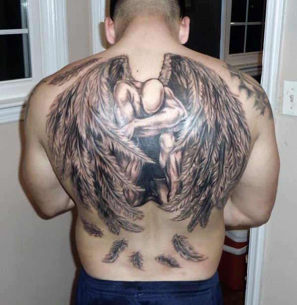 Full-back tattoo of a kneeling angel with large wings and scattered feathers