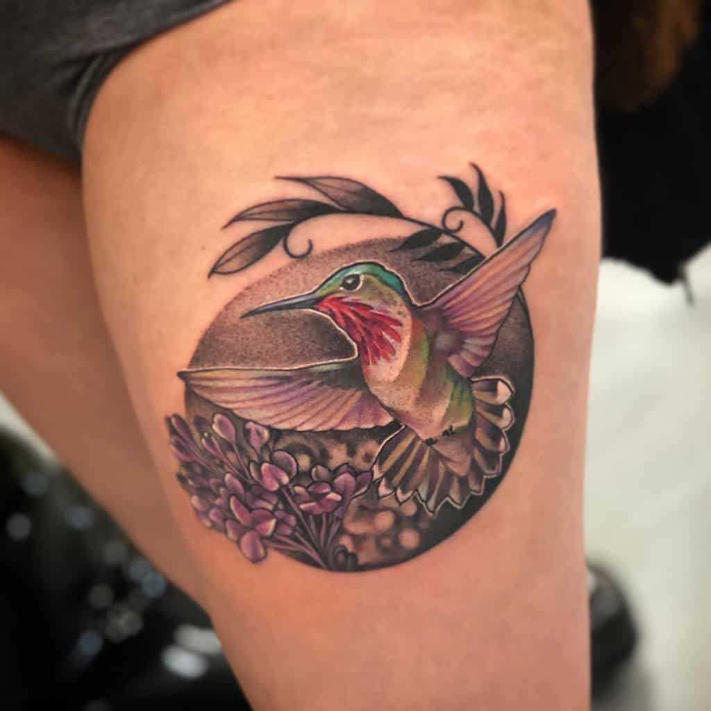 Realistic tattoo of a hummingbird in flight near lilac flowers, set against a circular background with soft shading and botanical details.