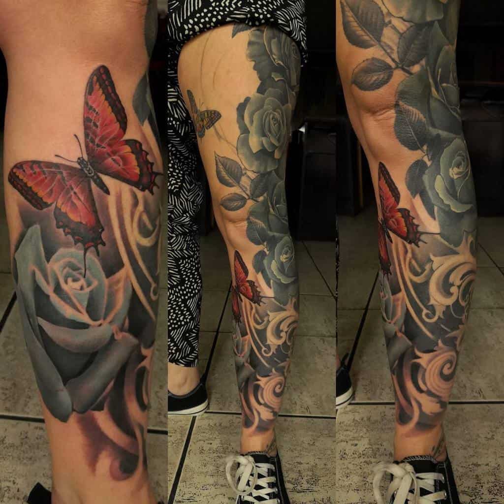 Close-up of a leg sleeve tattoo featuring blue roses with leaves and swirling patterns with a vibrant red butterfly