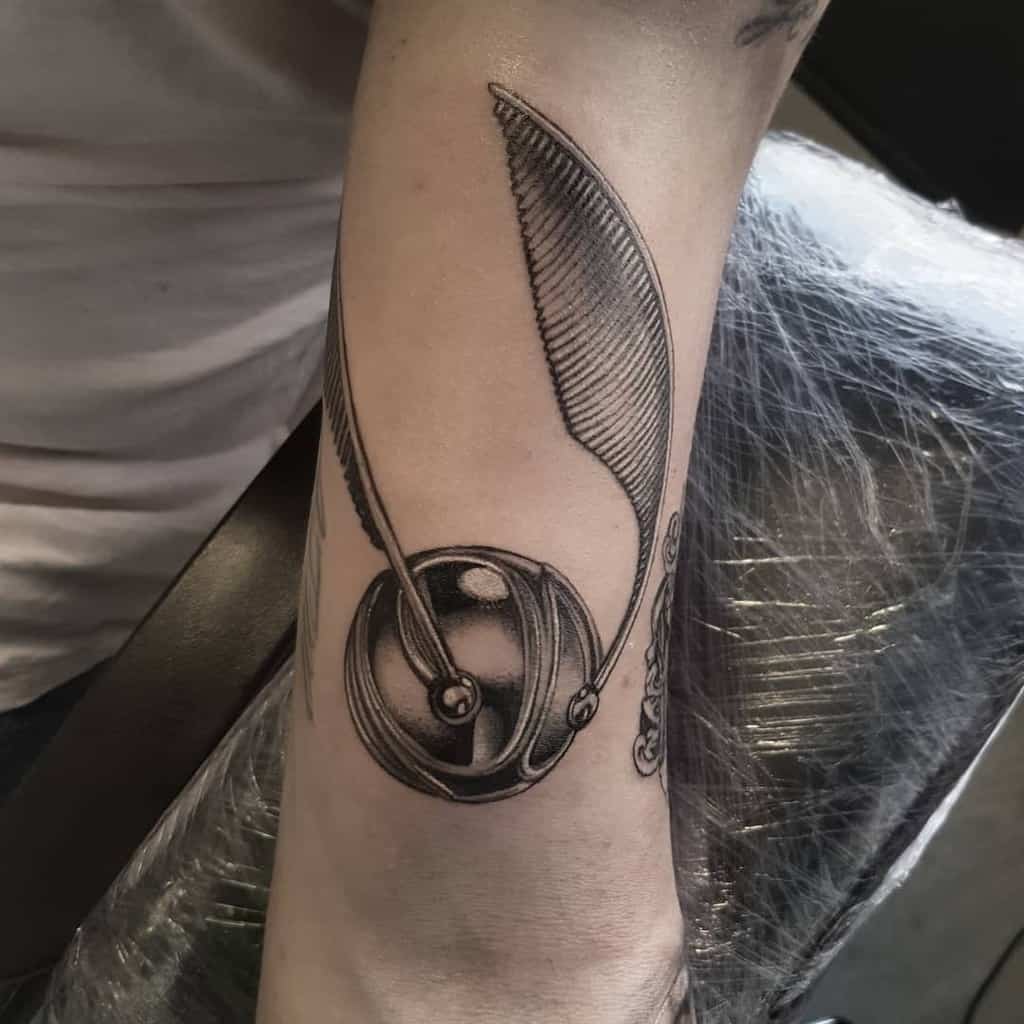 Detailed Harry Potter tattoo of the Golden Snitch in black and grey realism, with intricate shading and fine linework