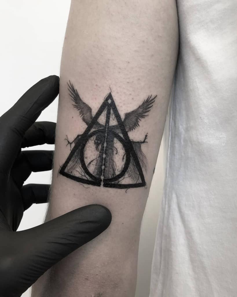 Dark, detailed Deathly Hallows tattoo with a grim figure inside the symbol, wings extending from the top, and intricate black ink shading.