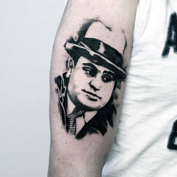 Al Capone tattoo on the arm featuring a black-and-white portrait of the gangster wearing his iconic fedora and a serious expression.