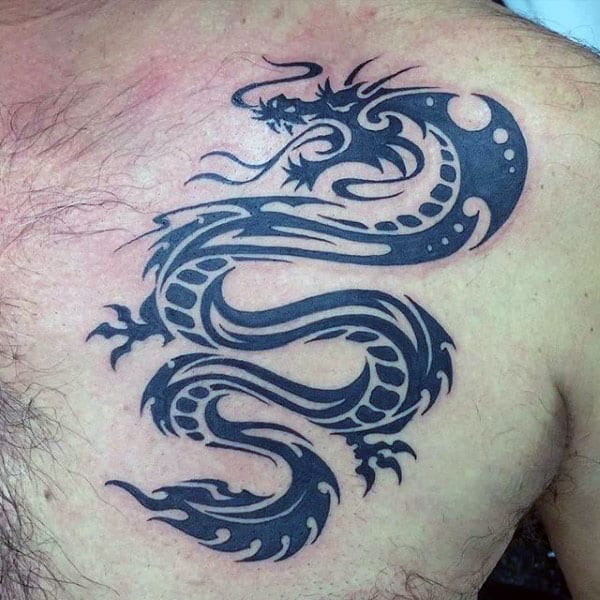Tattoo of an intricate black tribal dragon on a person's upper chest