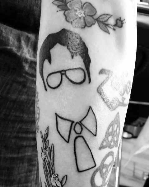 Minimalist black ink tattoo of Dwight Schrute featuring his iconic glasses, hair, and a stylized beet-inspired bowtie design on an arm.