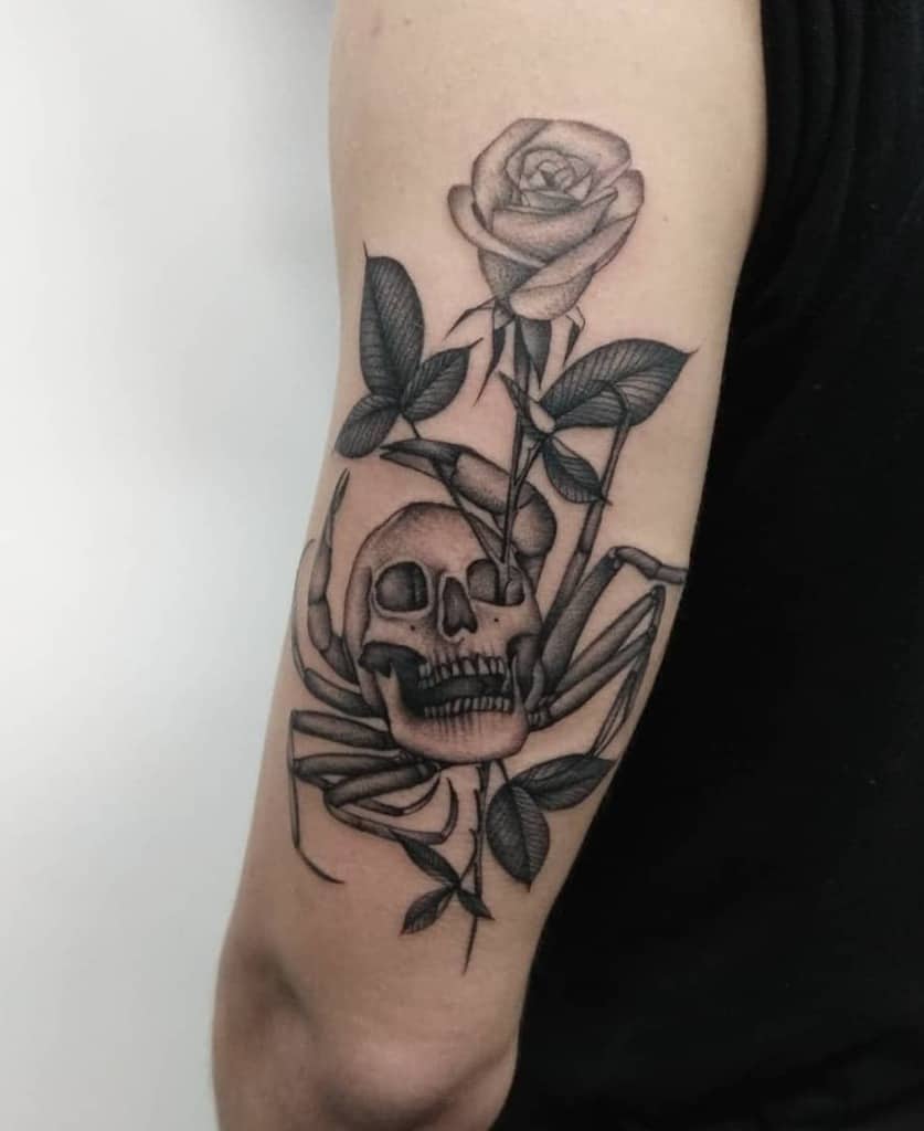 Black and grey tattoo of a spider with a skull body, intertwined with a detailed rose, creating a dark and artistic arm design.