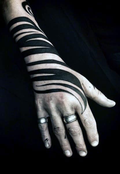 Hand with black geometric tattoo and rings on fingers, against a dark background