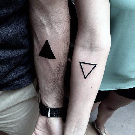 Minimalist couple tattoos with opposite triangle designs—one solid black and one outlined—symbolizing balance and complementarity.