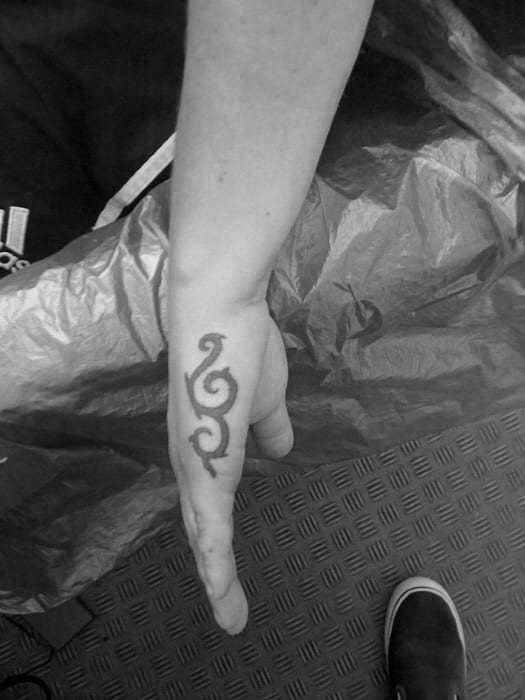 Side hand tattoo for men featuring a bold tribal swirl design running vertically along the outer edge of the hand.
