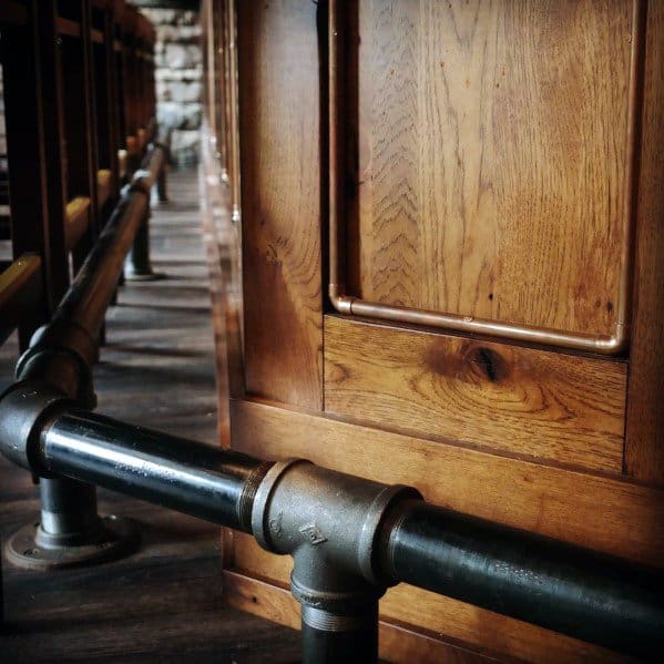 Black iron pipe foot rail attached to a wooden bar with dark wood flooring in a rustic environment.