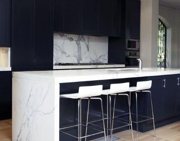 Black kitchen cabinets with marble countertops, waterfall island, and white bar stools.