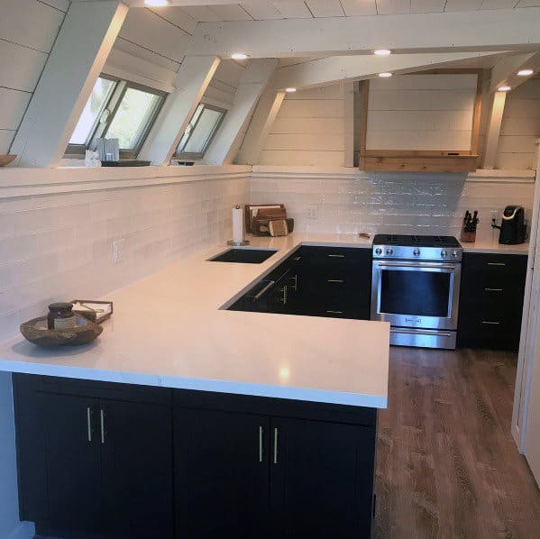 Black kitchen cabinets with white quartz countertops, wood accents, and slanted windows.